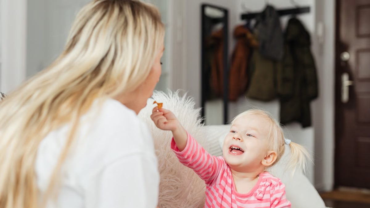 A heartwarming moment between a mother and her smiling child sharing a snack indoors.